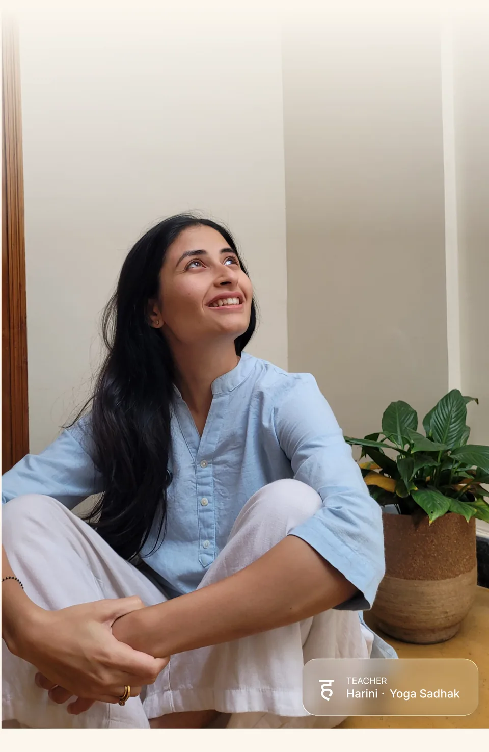Harini seated, looking upward, beside a potted plant
