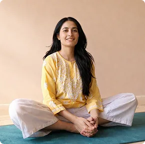 Harini seated cross-legged in a yellow kurta, smiling